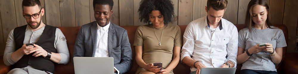 several people sitting on a bench all looking at phones or laptops