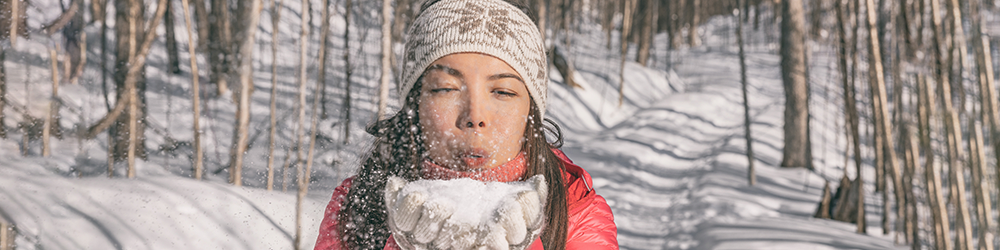 woman blowing snow from her hands in the woods