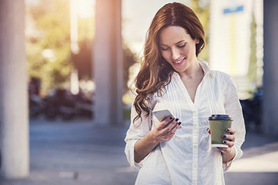 girl with coffee looking down at phone