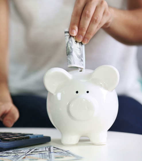 hand putting money in piggy bank with money and calculator
