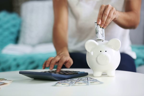 lady putting money into a piggy bank and using a calculator