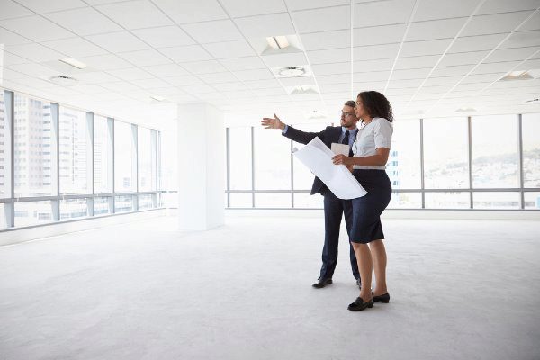 two business people in an empty office space with blue prints