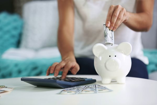 woman with calculator putting money in a piggy bank